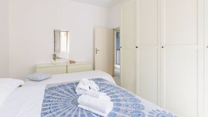 Een slaapkamer met een bed, nachtkastje met spiegel, inloopkast en een zichtbare badkamer door een open deur.