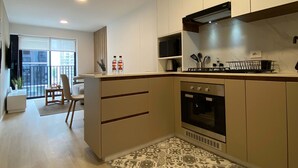 Una cocina moderna con horno empotrado, microondas y estufa a gas. Hay un comedor con una silla y una mesita.