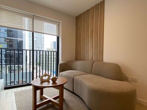 A modern living room with a sofa, a small wooden table, and a view of a cityscape through large windows. - w Serene Stay 2BR in San Isidro (Lima)