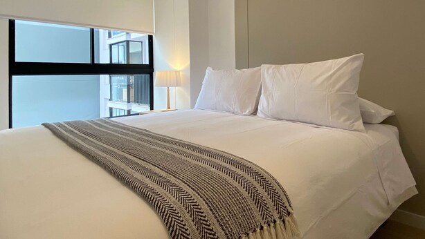 Una habitación de hotel moderna con una cama grande, vistas a la ciudad a través de una ventana y un diseño sencillo y limpio.