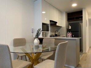 A modern kitchen with white cabinets, a glass dining table, and four chairs. - w Serene Stay 2BR in San Isidro (Lima)
