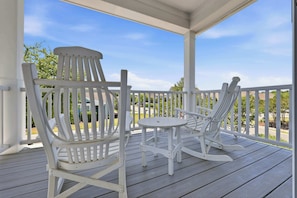 Eine überdachte Veranda mit zwei weißen Adirondack-Stühlen und einem kleinen runden Tisch.