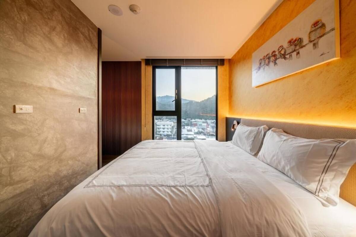 Habitació d'hotel moderna amb un llit gran, vista a la ciutat a través d'una porta corredissa i un quadre a la paret.
