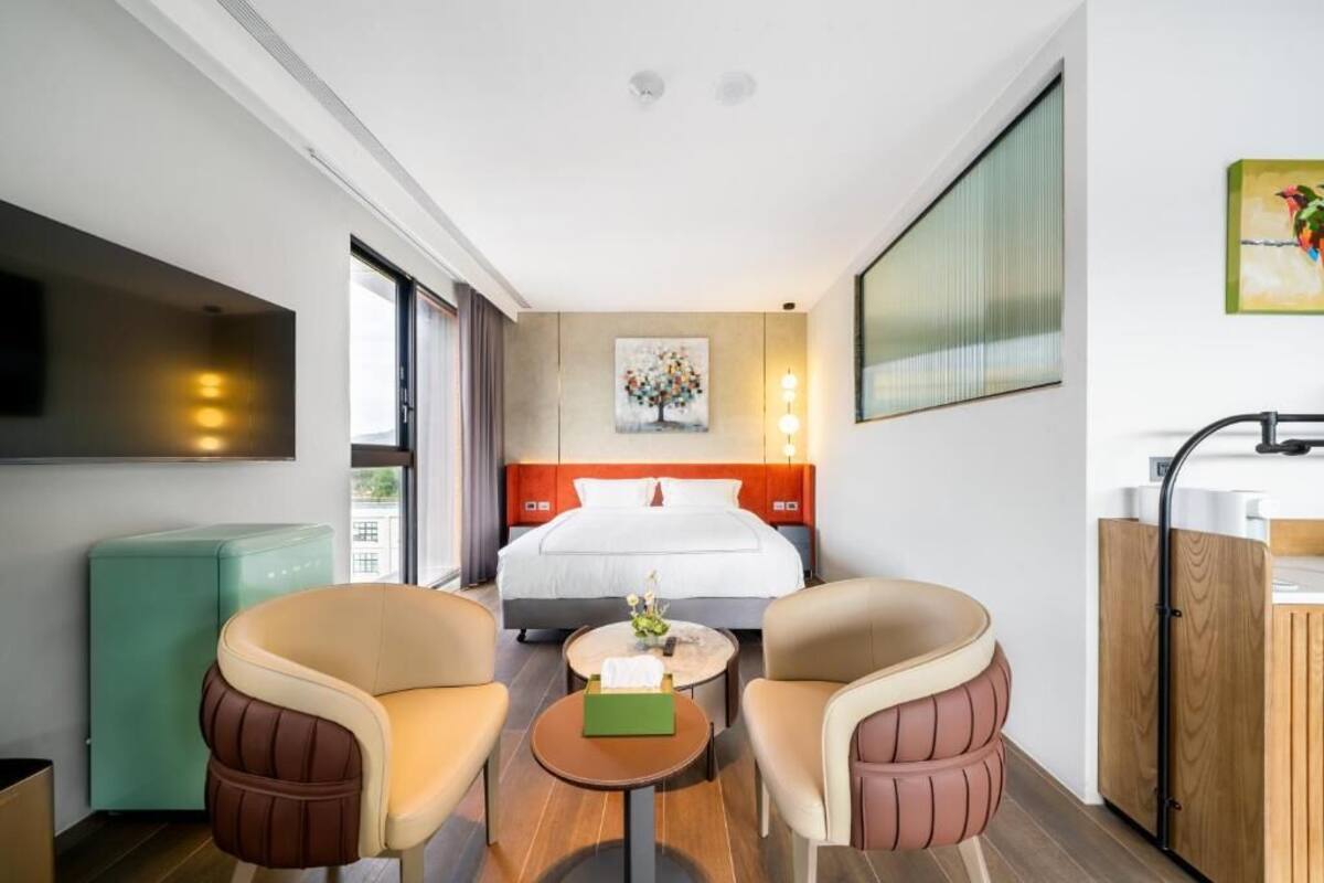 Habitació d'hotel amb un llit, dos seients, una taula rodona petita, un televisor, un quadre a la paret i una finestra.