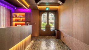 Un área de recepción con un mostrador de madera, una puerta de cristal con letrero de salida y un suelo de terrazo.