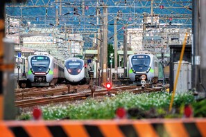 Three trains at a railway station with overhead electrical lines and tracks.