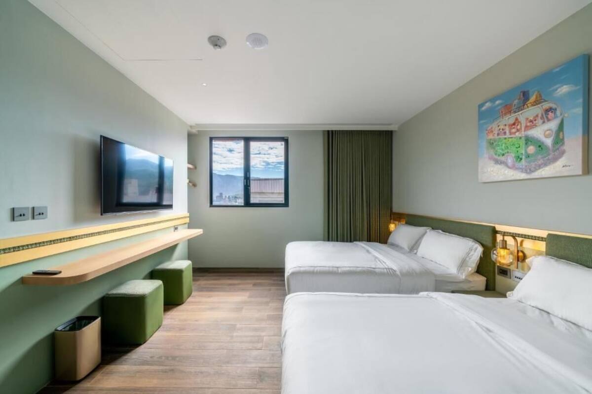 Habitació d'hotel amb dos llits, una televisió, un quadre i una finestra amb vistes.