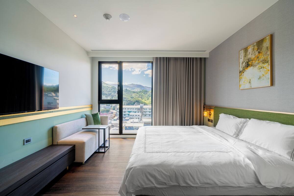 Una habitació d'hotel moderna amb un llit gran, una zona de seients, televisió de pantalla plana i vista a la ciutat.