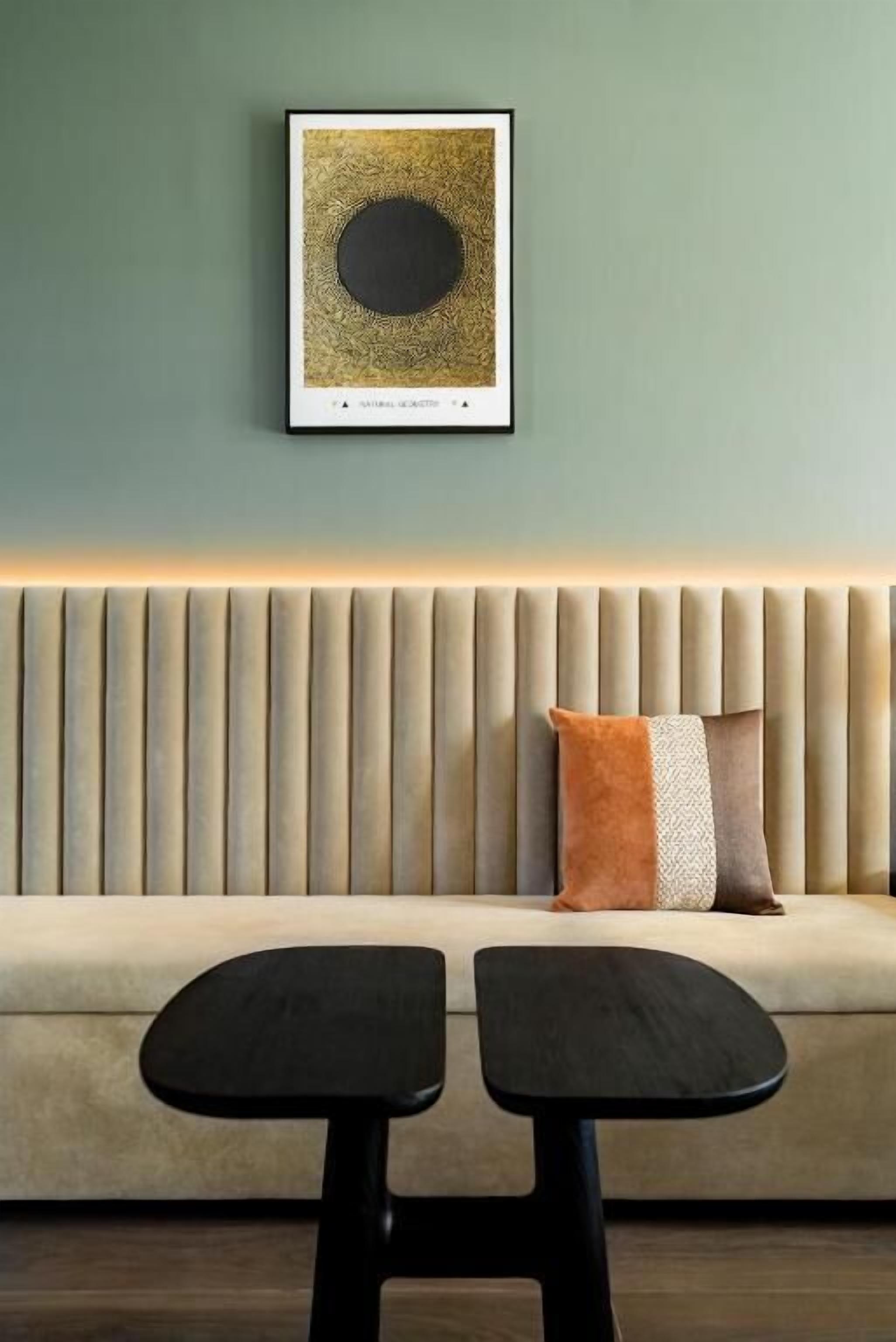A room with a sofa, two black stools, a framed artwork on the wall, and a textured wall panel.
