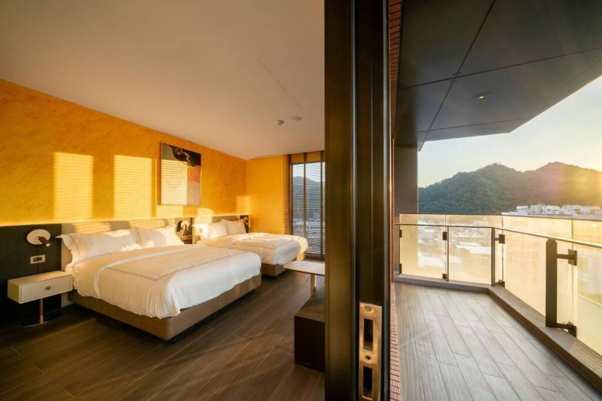 Habitació d'hotel moderna amb dos llits, un balcó i vistes a les muntanyes, i una finestra gran.