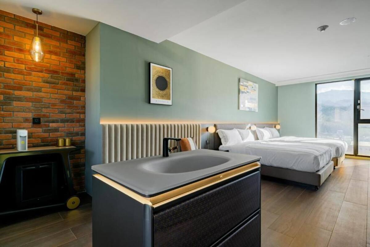 Habitació d'hotel moderna amb paret de detall de maó, un llit gran, taulell de treball integrat amb rentapans i vista a la ciutat.