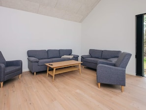 A modern living room with a grey sofa set, a wooden coffee table, and a large window providing natural light. - 5 Star Holiday Home in Ansager (Ansager)