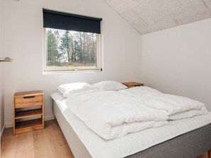 Ein Schlafzimmer mit einem Bett, einem Fenster mit Blick auf Bäume, einem Nachttisch aus Holz und einem Regal.