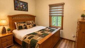 Un dormitorio con una cama de madera, una mesita de noche con lámpara, una ventana con persianas y un ventilador de techo.
