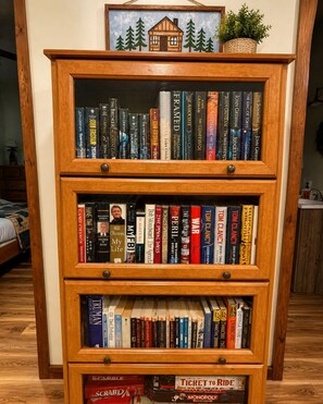 Uma estante de madeira com várias prateleiras, contendo livros e uma pequena moldura com a imagem de uma cabana.