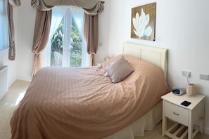 Ein Schlafzimmer mit einem Bett, einem Nachttisch, einer Lampe und einem Fenster mit Vorhängen.