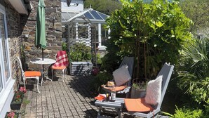 Un patio con dos sillas blancas, una mesa y un paraguas verde.