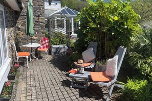 A patio with outdoor seating, a stone wall, and a greenhouse structure. - Coastal 1 Bed Flat - Sleeps 2 -patio - Parking (Boscastle)