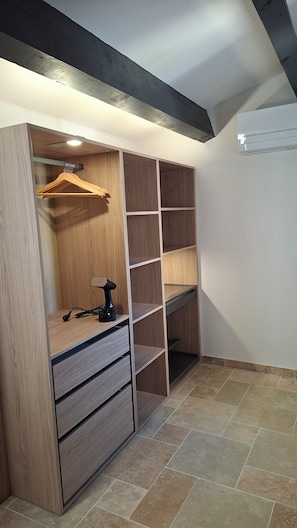 A walk-in closet with wooden shelving, a hanging rod, and a small table with a power strip. - Villa Colline St martin - Cap Agde (Agde)