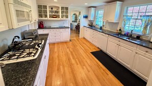 A kitchen with white cabinets, a gas stove, a microwave, and a window with curtains. - Harwich Port Walk to Beach and Village Beautiful 4 Bedroom, 3.5 Bath Home (Harwich Port)