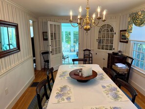 Ein Esszimmer mit einer Kronleuchter, Tischdecken mit Blumenmuster und Blick ins Freie.