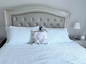Ein Bett mit einer gesteppten Kopfteil, zwei Kissen und ein Nachttisch mit Lampe und Vase.