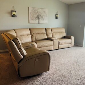 Ein beiges Ecksofa in einem Wohnzimmer mit hellem Teppich, einem Wandbild und zwei Wandleuchten.