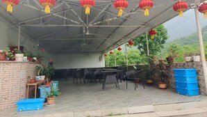 A covered outdoor area with tables and chairs, red lanterns, potted plants, and a blue storage bin. - Country Inn Mutianyu Jiankou Great Wall (Huairou)