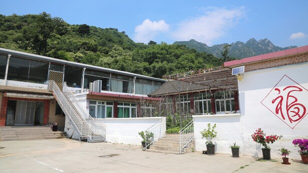 A building with a staircase, a wall with a red symbol, and a mountain in the background. - Country Inn Mutianyu Jiankou Great Wall (Huairou)