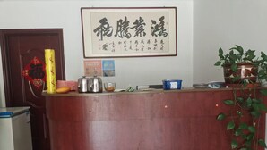 A reception desk with a framed Chinese calligraphy piece, a red decorative hanging, and a potted plant. - Country Inn Mutianyu Jiankou Great Wall (Huairou)