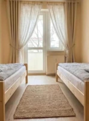 Ein Schlafzimmer mit zwei Betten, einem Fenster mit Vorhängen, einem Heizkörper und einem Teppich.