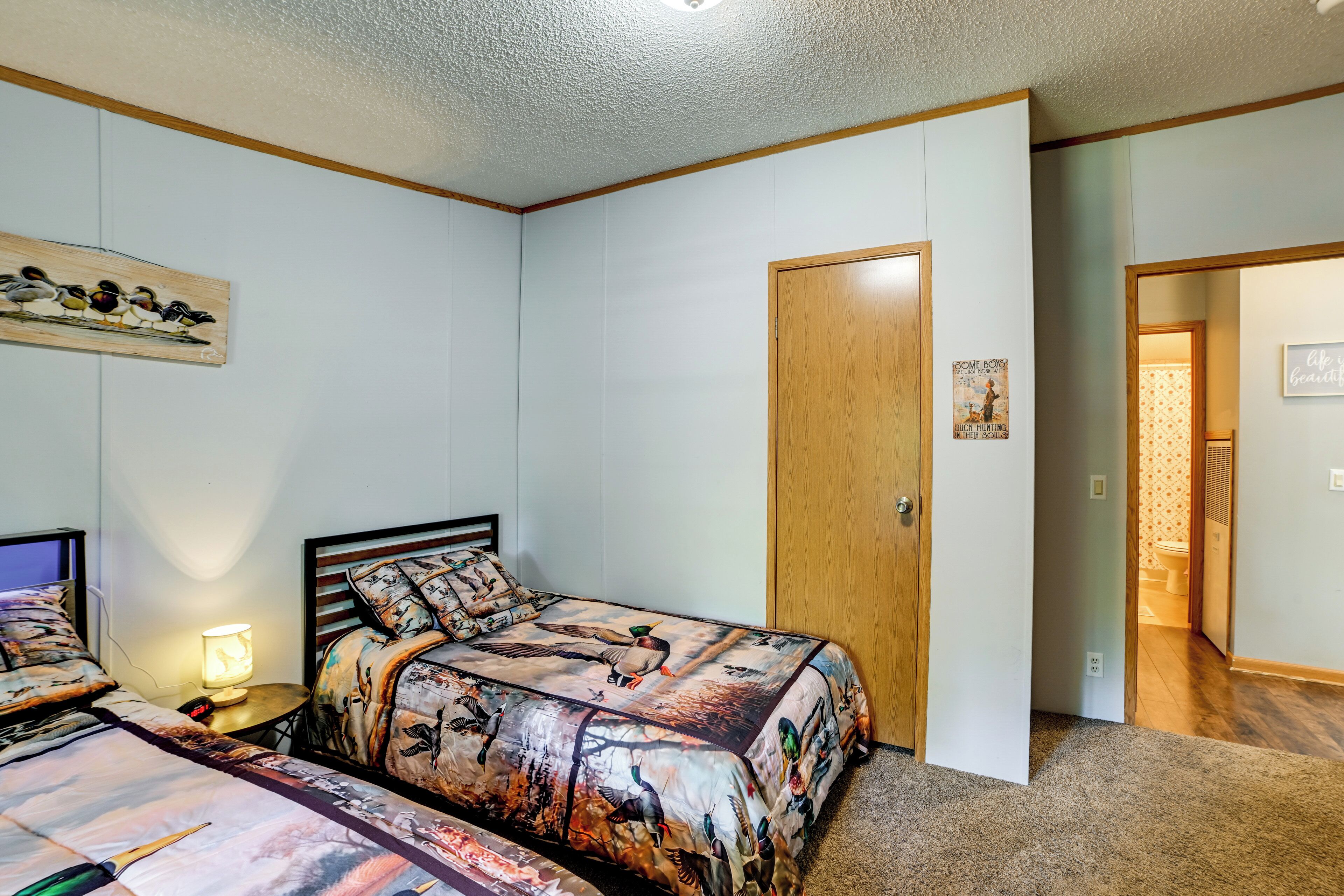 Un dormitorio con dos camas, una puerta de madera, una lámpara de pared y un cartel.