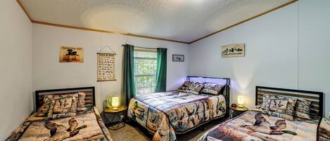 A bedroom with three beds, each with a hunting-themed bedspread, a window with curtains, and wall art.