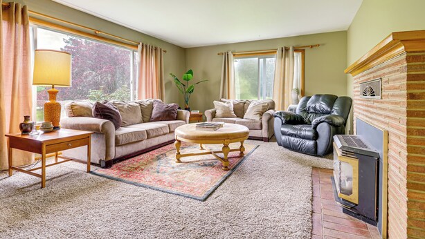 Ein Wohnzimmer mit Sofa, Sesseln, Hocker und Kamin.