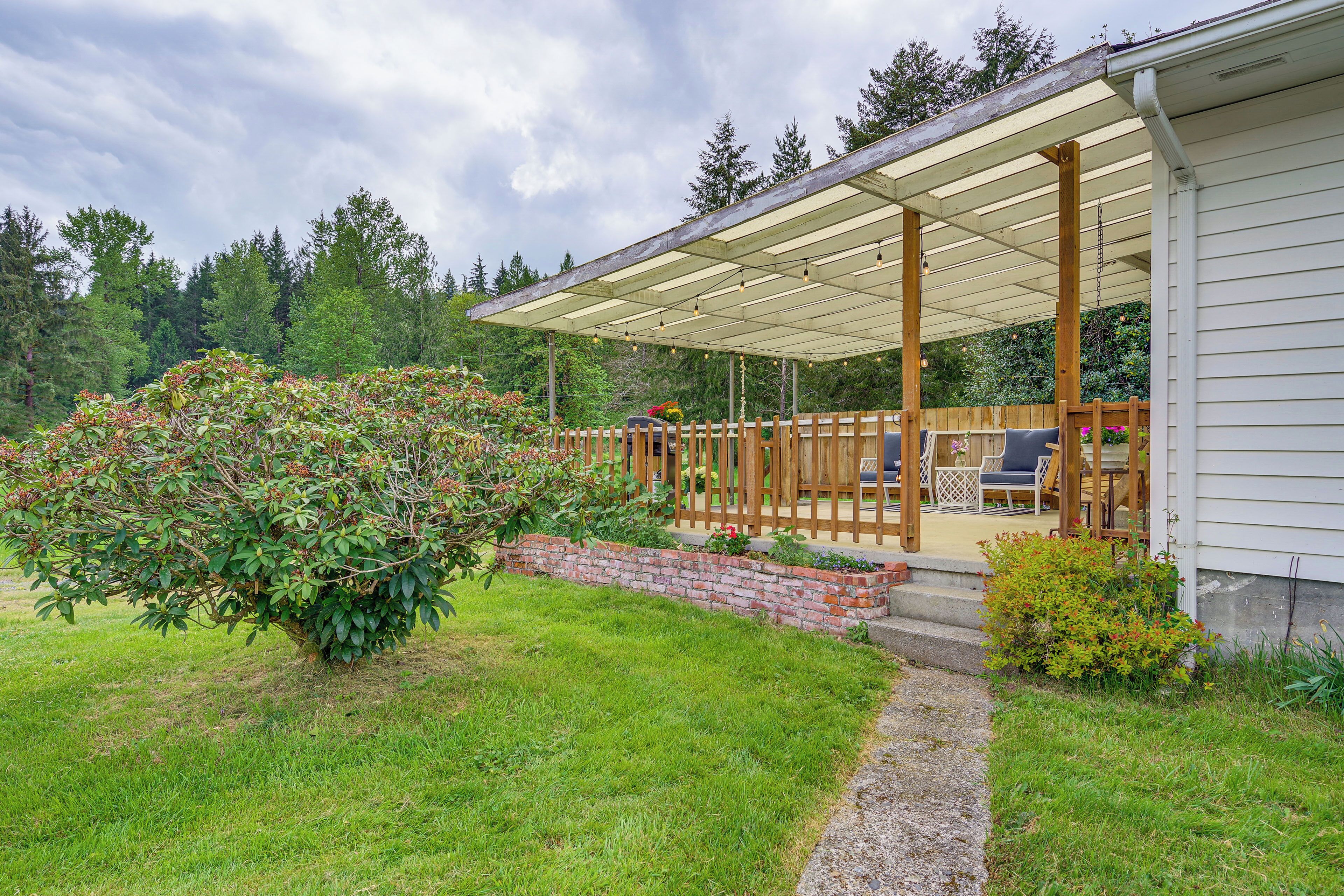 Un patio techado con mobiliario exterior, una jardinera de ladrillo y una valla de madera.