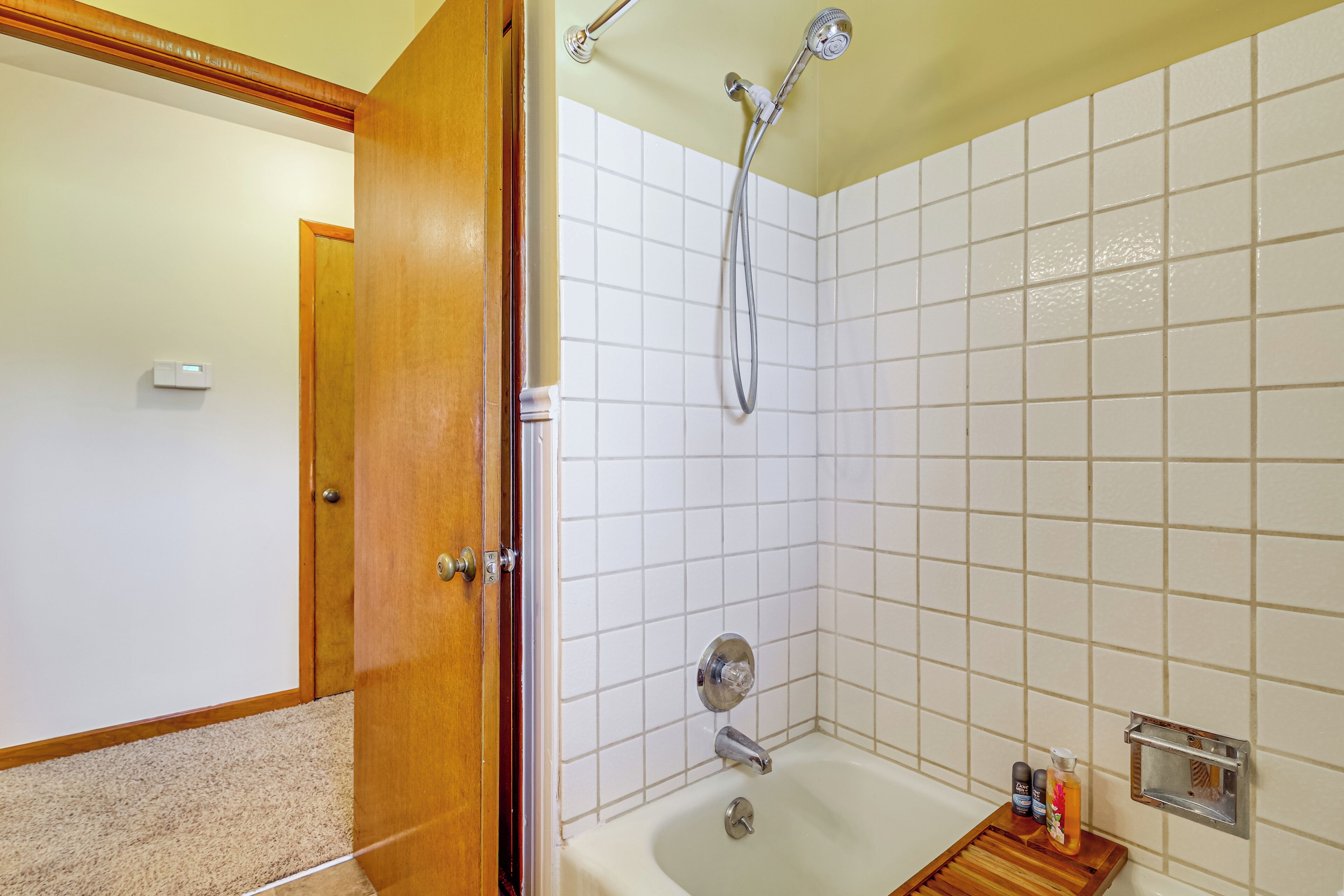 A bathroom with a bathtub, a shower, and a wooden shelf with toiletries.