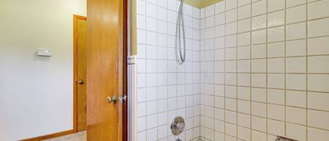 A bathroom with a bathtub, a shower, and a wooden shelf with toiletries.