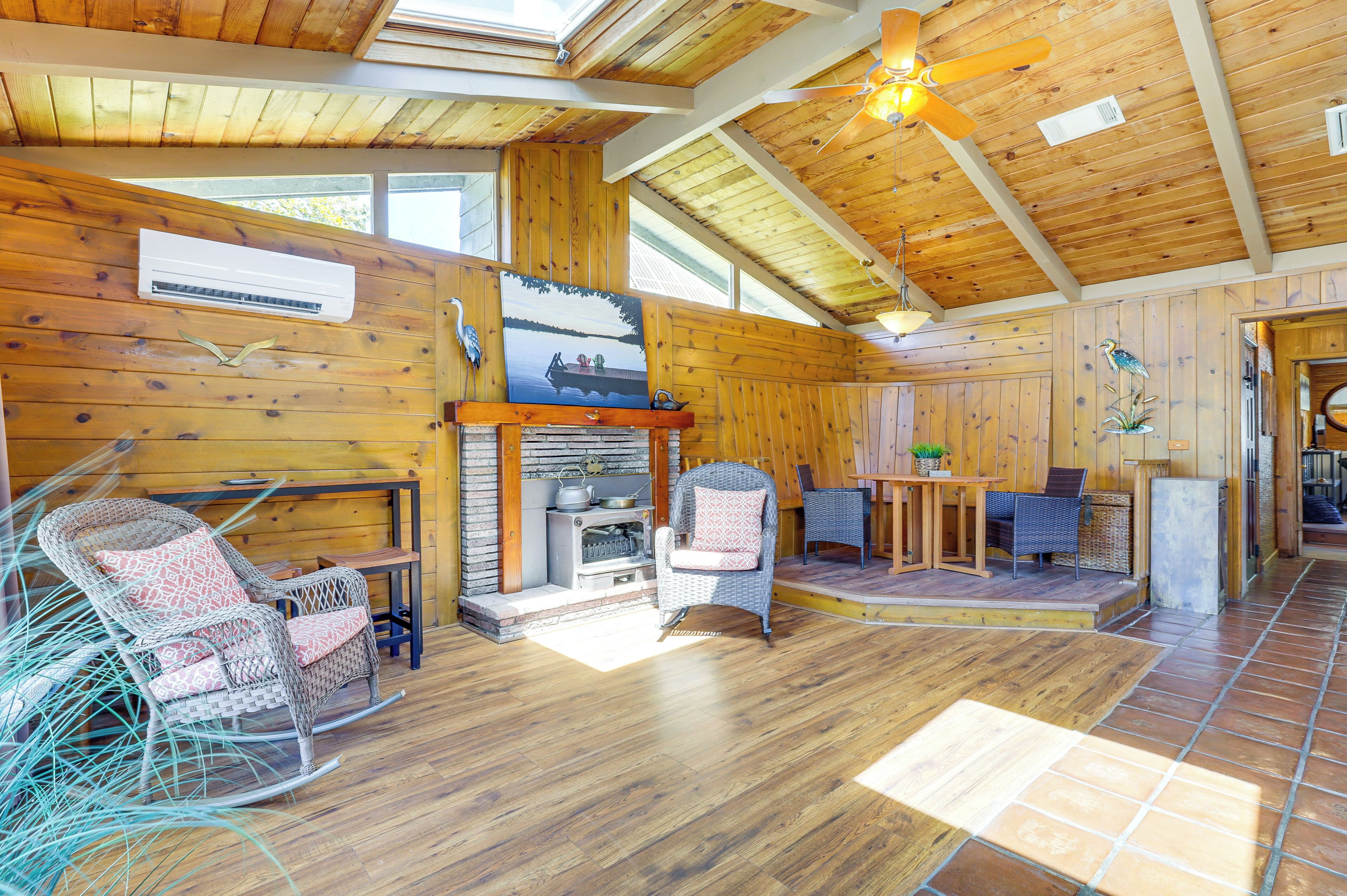 Un intérieur en bois avec une cheminée, des meubles en osier et un ventilateur de plafond.