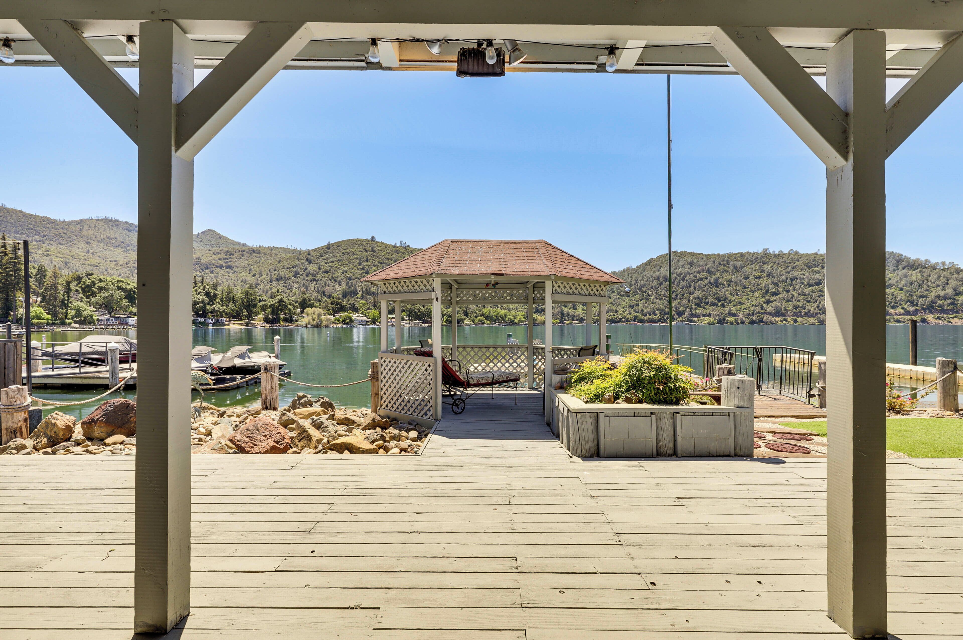 A wooden deck with a gazebo, a dock with boats, and a lake with hills in the background.
