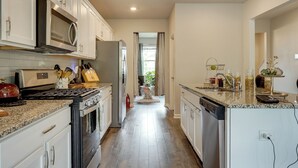Une cuisine moderne avec des armoires blanches, un comptoir en granit, des appareils électroménagers en acier inoxydable et une vue sur la salle à manger.