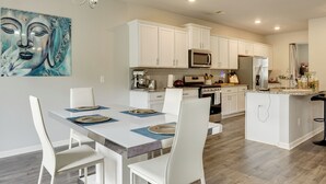Une cuisine moderne avec des meubles blancs, une table à manger avec des chaises et un îlot central doté de tabourets de bar.