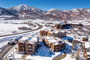 Ein schneebedecktes Resort mit mehreren Holzhäusern, einer kurvenreichen Straße und Bergen im Hintergrund.