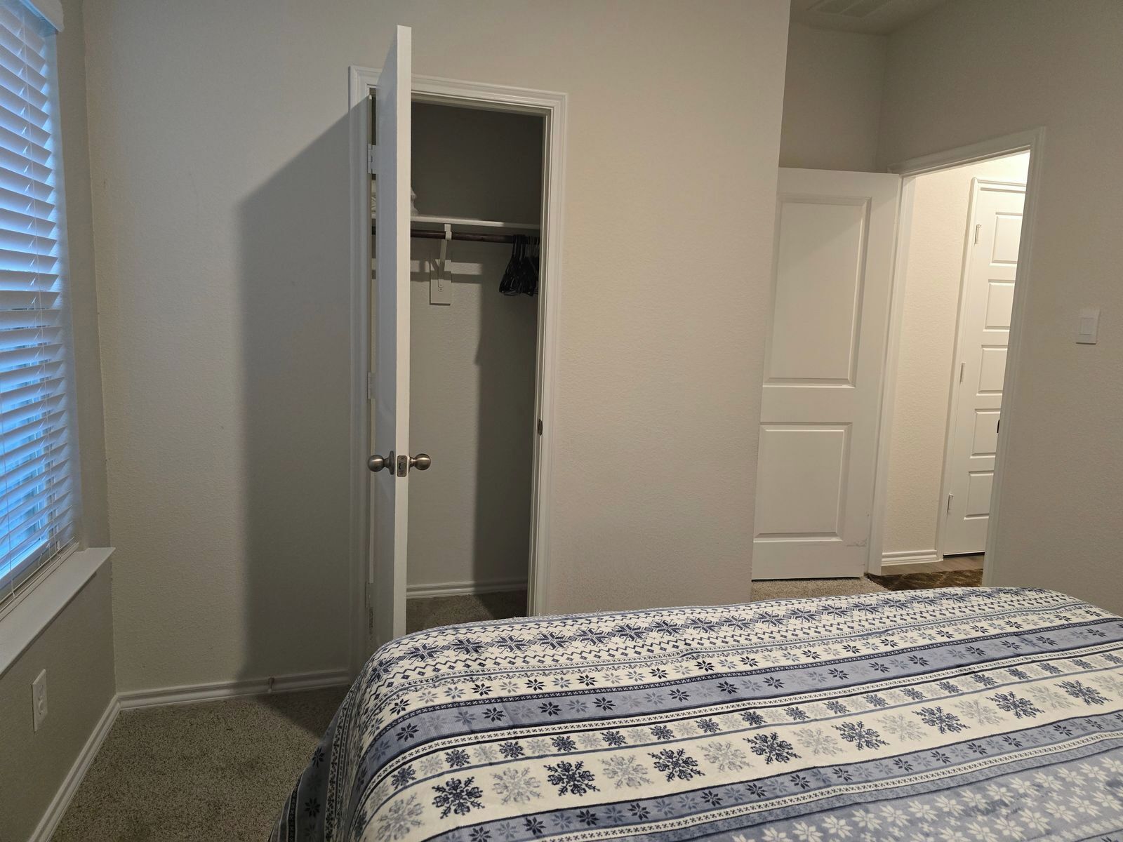A bedroom with a bed, an open closet, and a door leading to another room.