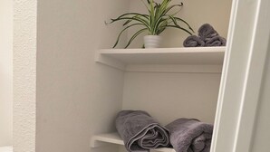 Ein Eckschrank mit weißen Wänden, eine Topfpflanze auf der obersten Ablage und ordentlich gefaltete Handtücher in den Schränken.