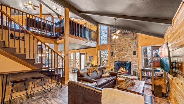 A spacious interior with a stone fireplace, a wooden staircase, and a cozy seating area. - Sleeps 14! Hot Tub*Resort Amenities*Arcade*Games (Gatlinburg)