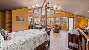 A spacious loft bedroom with a large bed, a cozy seating area, and a view of the outdoors through large windows. - Sleeps 14! Hot Tub*Resort Amenities*Arcade*Games (Gatlinburg)