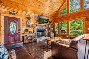 Ein gemütliches Blockhaus-Interieur mit Kamin, Holzwänden und einem großen Fenster mit Blick ins Freie.