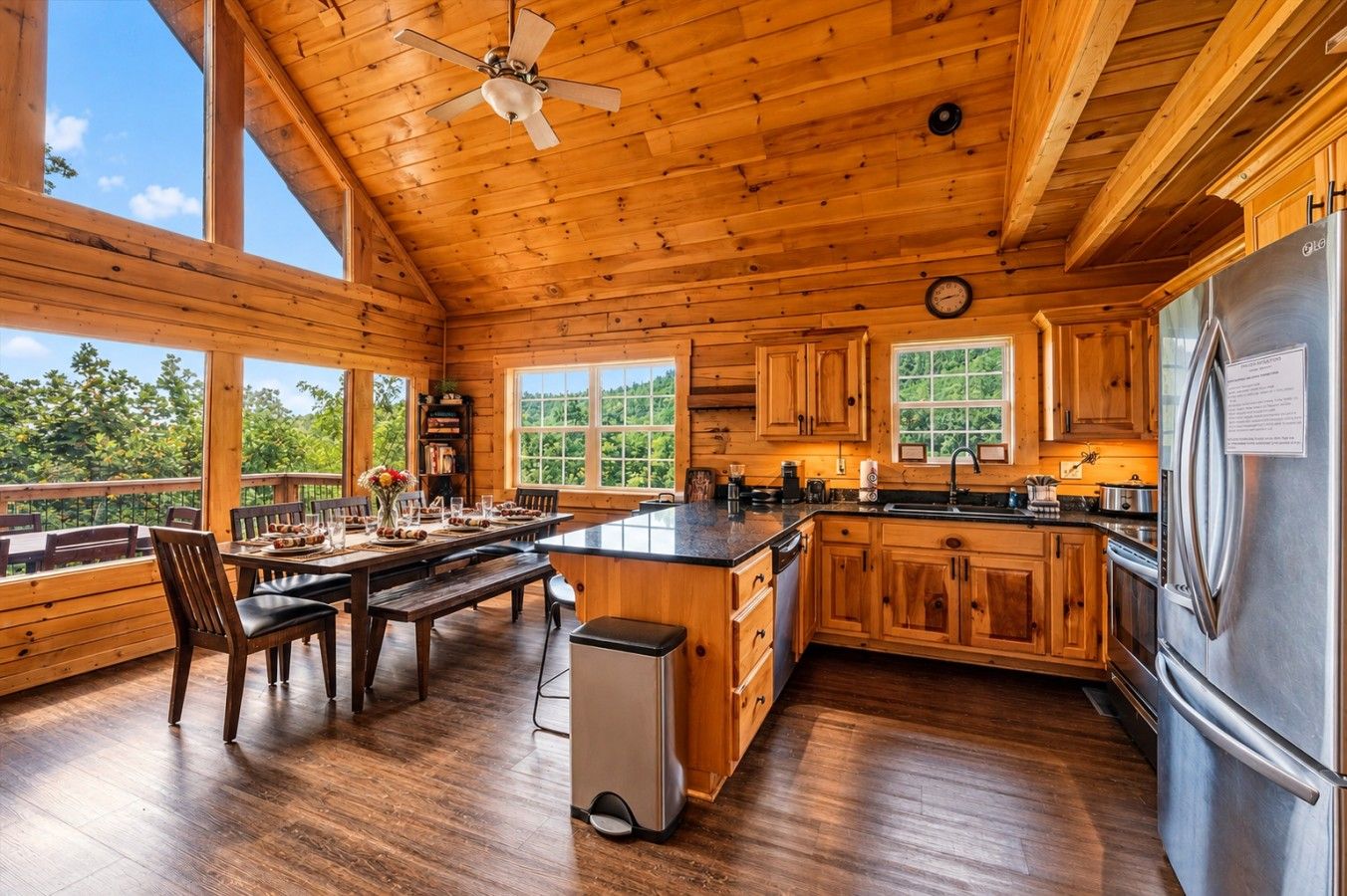 A spacious wooden cabin with a large dining area, kitchen, and a view of the outdoors.