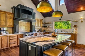 A kitchen with a large island, wooden cabinets, a gas stove, and pendant lighting. - Luxury Lakefront! 5BR*Lake Access*Hot Tub*Private! (Sevierville)