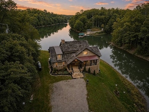 A house with a stone foundation, a gravel driveway, and a river in the background. - Luxury Lakefront! 5BR*Lake Access*Hot Tub*Private! (Sevierville)